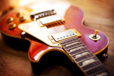 Red sunburst color single cutaway electric solid body guitar, on a old grungy wooden surface. Shallow depth of field.
